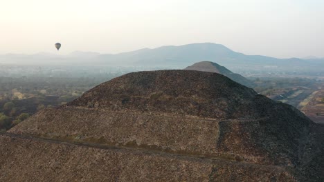 Aerial-view-of-hot-air-baloon-flying-between-Pyramid-of-the-Moon-and-pyramid-of-the-Sun-in-ancient-mesoamerican-city-of-Teotihuacan,-Mexico-from-above,-Central-America,-sunrise,-4k