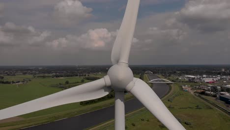 Stetige-Luftaufnahme-Einer-Einzelnen-Windkraftanlage-Mit-Rotierenden-Flügeln,-Die-Strom-Erzeugen,-Und-Einer-Holländischen-Wasserstraßenlandschaft-Im-Hintergrund