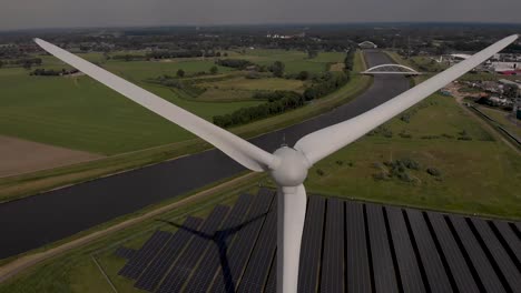 Closeup-aerial-of-wind-turbine-blades-and-solar-panels-in-The-Netherlands-Dutch-flat-landscape-with-Twentekanaal-and-bridges-in-the-background