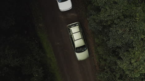 4k-Drone-top-down-view-of-white-cars-parked-on-a-dirt-road-in-a-green-forest-in-Australia