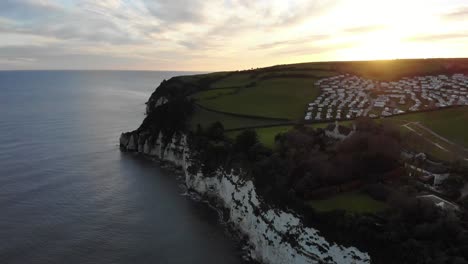 4k-Langsame-Luftaufnahme-über-Dem-Meer-Und-Den-Klippen,-Die-Den-Wunderschönen-Sonnenuntergang-über-Der-Stadt-Bier-In-Devon-England-Zeigen
