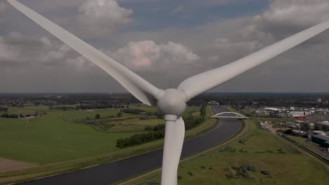 Rotating-blades-aerial-closeup-approach-of-wind-turbine-with-Dutch-waterway-infrastructure-Twentekanaal-in-flat-landscape
