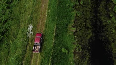 Bird's-Eye-View-Of-A-Red-Truck-Traveling-On-a-Rough-Road-Surrounded-With-Greenfields