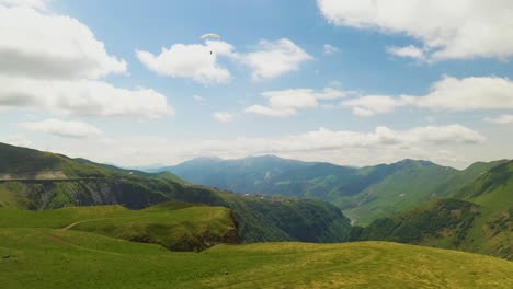 Wide-cinematic-drone-shot-of-paraglider-flying-in-the-Caucasus-mountains-in-Gudauri-Georgia-rotating-and-revealing-the-valley