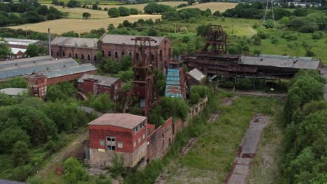 Abandoned-old-overgrown-coal-mine-industrial-museum-buildings-aerial-view-pull-back-slow