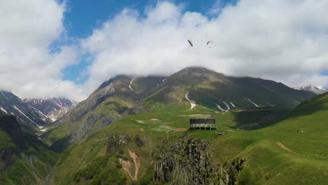 Cinematic-drone-shot-of-the-Caucasus-mountains-with-the-Arch-of-Friendship-of-Peoples-in-the-distance-with-people-paragliding