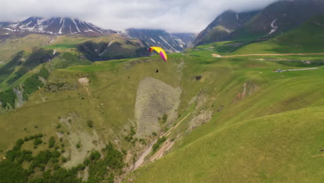 Wide-rotating-drone-shot-of-paraglider-flying-in-the-Caucasus-mountains-in-Gudauri-Georgia