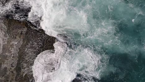 Aerial-top-down-rising-over-sea-waves-crashing-on-rocky-coast