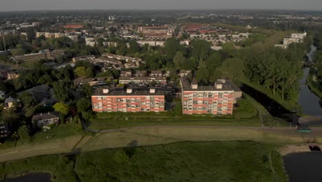 Aerial-approach-of-cityscape-with-closed-orange-sunshades-of-high-rise-apartment-buildings-along-river-IJssel-in-slow-backwards-movement-revealing-Dutch-floodplains-landscape-in-Zutphen