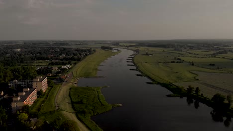 Sunset-aerial-cityscape-following-river-valley-of-the-IJssel-waterway-in-slow-backwards-movement-revealing-bucking-and-residential-neigbourhood-and-floodplains-of-tower-town-Zutphen-in-The-Netherlands