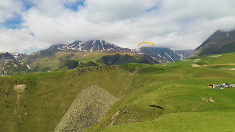 Wide-drone-shot-of-a-paraglider-in-Gudauri-Georgia-with-the-Caucasus-mountains-in-the-distance