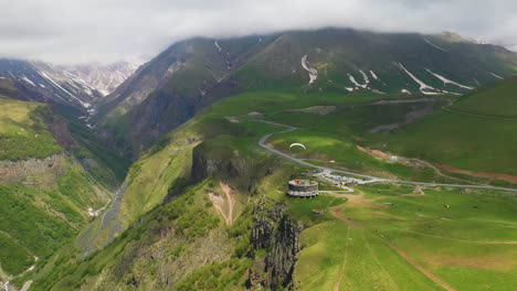 Wide-drone-shot-of-paraglider-flying-near-the-Arch-of-Friendship-Of-Peoples-in-Gudauri-Georgia
