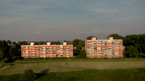 Sonnenuntergang-Luftstadtbild-Mit-Wohnhochhäusern-Mit-Geschlossenem-Orangefarbenem-Sonnenschirm-Entlang-Des-Flusses-Ijssel-In-Langsamer-Rückwärtsbewegung,-Die-Die-Niederländische-Überschwemmungslandschaft-In-Zutphen,-Niederlande,-Enthüllt