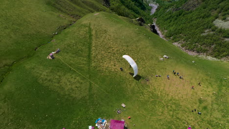 Downward-angle-drone-shot-of-a-paraglider-landing-on-a-mountaintop-in-Gudauri-Georgia