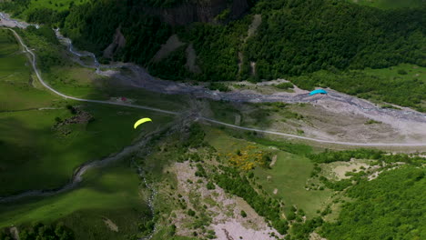 Downward-angle-drone-shot-of-a-paraglider-flying-through-a-valley-in-Gudauri-Georgia
