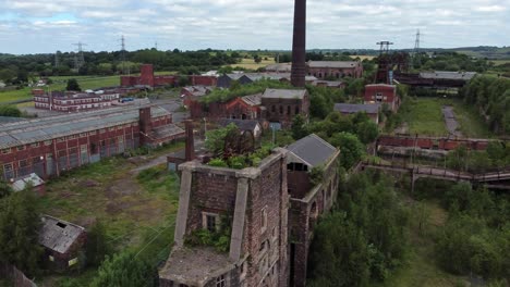 Abandoned-old-overgrown-coal-mine-industrial-rusting-pit-wheel-ruin-aerial-view-descending-pull-back