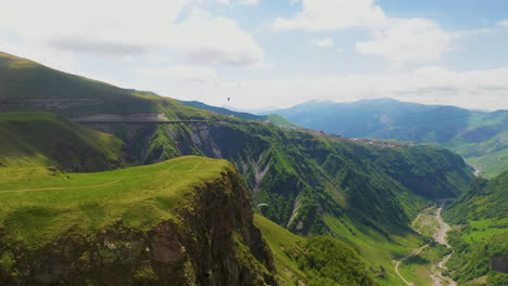Wide-drone-shot-of-the-Caucasus-mountains-with-people-paragliding-in-the-distance-in-Gudauri-Georgia