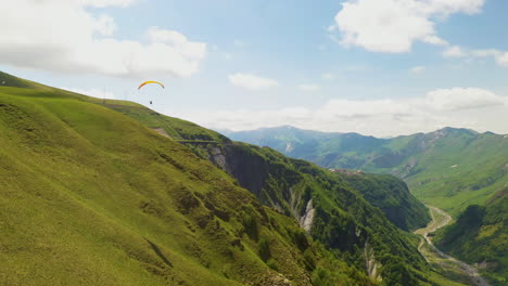 Wide-drone-shot-of-paraglider-flying-in-the-Caucasus-mountains-in-Gudauri-Georgia-rotating-and-revealing-the-valley