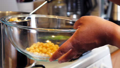 Black-person's-hands-seen-spooning-out-chickpeas-from-the-boiling-pot-into-a-glass-bowl