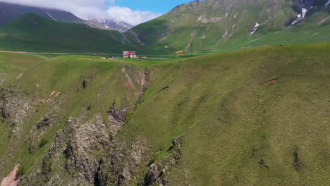 Wide-rotating-drone-shot-of-paraglider-flying-near-a-cliff-in-the-Caucasus-mountains-in-Gudauri-Georgia