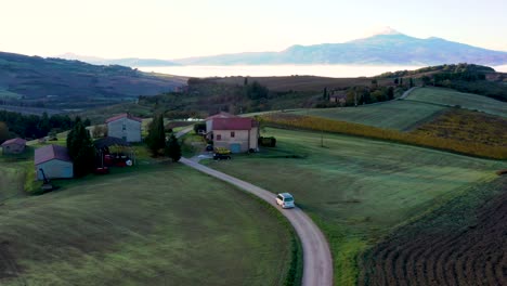 4K-Drone-aerial-footage-of-a-car-,-van-moving-on-empty-road-in-autumn-fields-during-sunrise-in-Tuscany,-Italy
