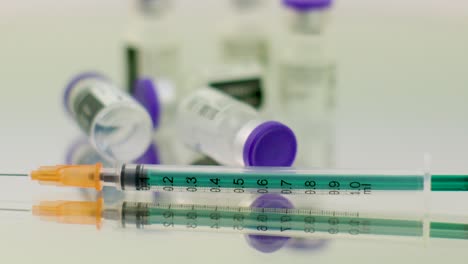 Close-up-of-a-green-syringe-and-a-few-coronavirus-vaccine-bottles