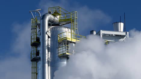Steel-tank-tower-in-a-chemical-refinery-covered-by-smoke-against-the-blue-sky