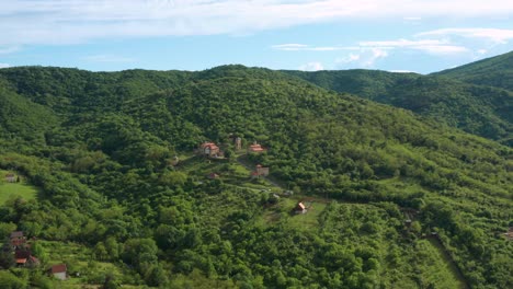Schöne-Aussicht-Auf-Grüne-Hügel,-Die-Von-Bäumen-Bedeckt-Sind-Und-Eine-Kleine-Siedlung-Mit-Orangefarbenen-Häusern-Umgeben---Luftdrohnenaufnahme