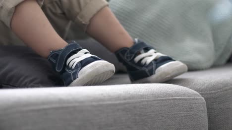 Cute-Child-Shoes-On-Sofa,-Blue-Sneakers-On-Gray-Sofa,-Close-Up
