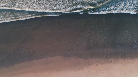 Top-down-view-of-waves-hitting-shore,-shot-by-drone
