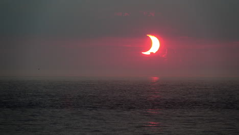 Crescent-shaped-sun-at-dawn,-during-a-partial-solar-eclipse,-rises-over-ocean