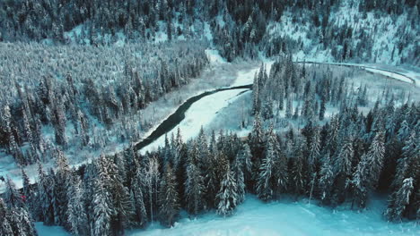 Luftaufnahme-Des-Zuges,-Der-Im-Winter-Durch-Gefrorenen-Wald-Und-Fluss-Im-Glacier-National-Park-Fährt