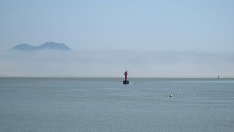 Red-buoy-in-the-Yellow-Sea,-Mountain-Covered-in-Dense-White-Haze-Near-Ganghwado-Island,-South-Korea