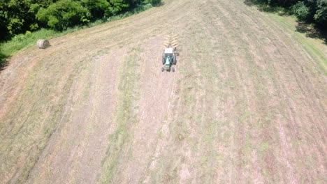 Drone-aerial-view-of-tractor-pulling-a-rake-through-a-hay-field-to-make-windrows-for-later-baling-in-western-Illinois-during-early-summer