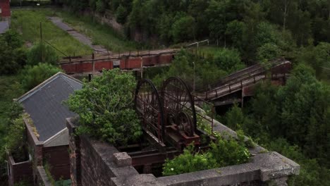 Abandoned-old-overgrown-coal-mine-industrial-rusting-pit-wheel-aerial-view-orbit-right