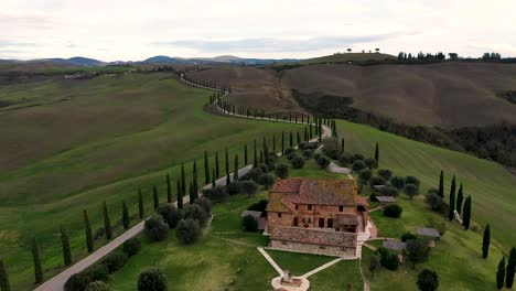 Tuscany-countryside-aerial-shot-with-drone-at-sunset-time---farmhouse,-hills-fields,-vineyards,-cypress-trees-along-white-road