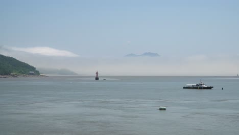 Fisherman's-ship-in-the-Yellow-Sea-and-Red-navigational-buoy-floating-between-islands,-a-mountain-covered-in-dense-haze,-Ganghwado-island,-South-Korea,-static-wide
