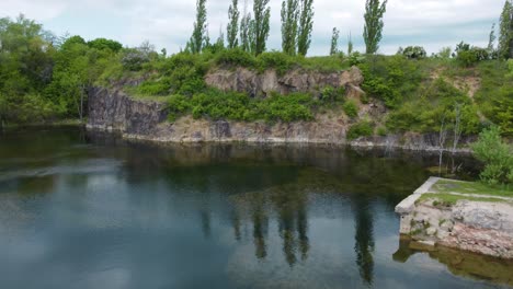 flying-over-a-flooded-quarry-full-of-algae-towards-a-cliff-with-trees-above-it