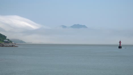Boya-De-Navegación-Roja-Flotando-En-El-Mar-Amarillo-Entre-Islas,-Una-Montaña-Cubierta-De-Nubes-De-Niebla-Cerca-De-La-Isla-De-Ganghwado,-Corea-Del-Sur-Tiro-Amplio-Estático