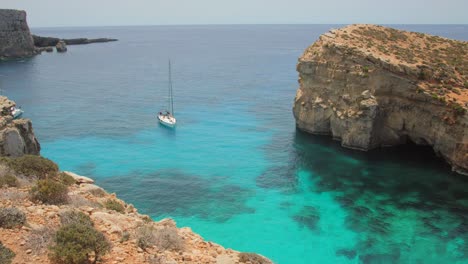 Sailboat-near-the-cliffs-of-the-island-of-Comino-with-its-crystal-clear-blue-waters