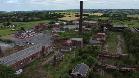 Abandoned-old-overgrown-coal-mine-industrial-museum-buildings-aerial-view-rising-pull-back