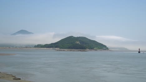 Ganghwado-Island-Mountains-Covered-with-Dense-Mist-Clouds-Surrounded-with-Yellow-Sea-water-in-South-Korea,-Red-navigational-buoy-floating,-ebb-tide,-low-tide