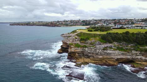 Waves-Crashing-At-Rocky-Cliff-Of-Mackenzies-Point-With-Tourists-At-Marks-Park-In-Tamarama,-NSW,-Australia