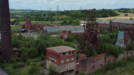 Abandoned-old-overgrown-rusting-coal-mine-industrial-wheel-buildings-aerial-view-dolly-right