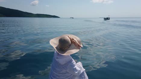 Woman-tourist-wearing-summer-hat-sitting-on-a-boat-edge-and-pointing-her-finger-forward