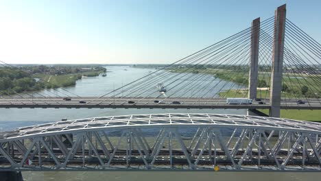 Fliegen-Parallel-Zur-Autobahnbrücke-Und-Eisenbahnbrücke-Mit-Boot,-Das-Den-Fluss-Im-Hintergrund-An-Einem-Klaren-Sonnigen-Tag-überquert