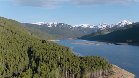 Luftdrohne-Malerische-Landschaft-Des-Seereservoirs-Im-Kiefernwald-In-Den-Schneebedeckten-Felsigen-Bergen-Von-Colorado