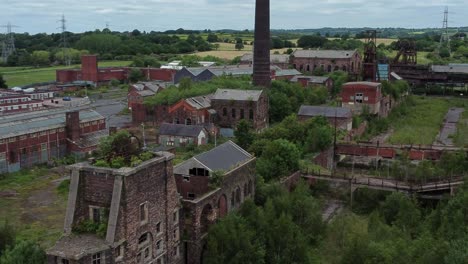Abandoned-old-overgrown-countryside-coal-mine-industrial-museum-buildings-aerial-view-zoom-in