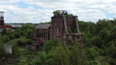 Abandoned-old-overgrown-coal-mine-industrial-rusting-pit-wheel-buildings-aerial-view-rising-tilt-down