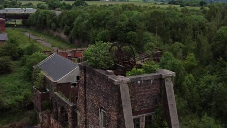 Abandoned-old-overgrown-coal-mine-industrial-rusting-pit-wheel-aerial-view-rising-over
